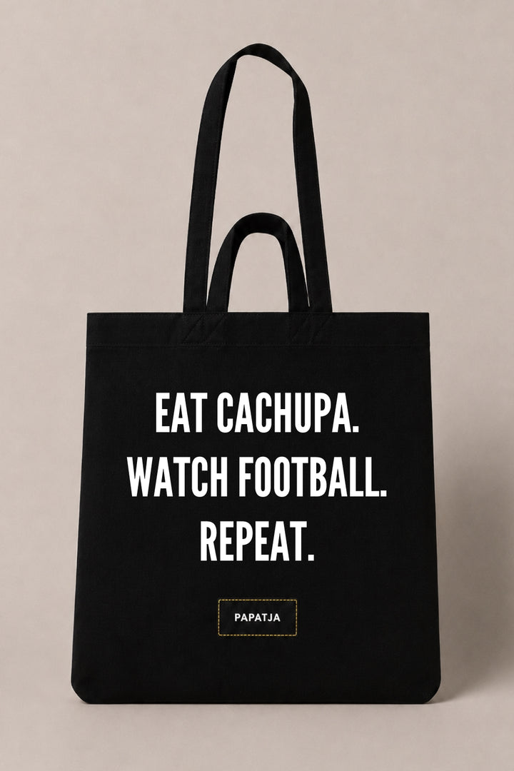 Zwarte katoenen PAPATJA tas met de tekst Eat Cachupa. Watch Football. Repeat., voor Cabo Verde fans die houden van voetbal en cachupa.