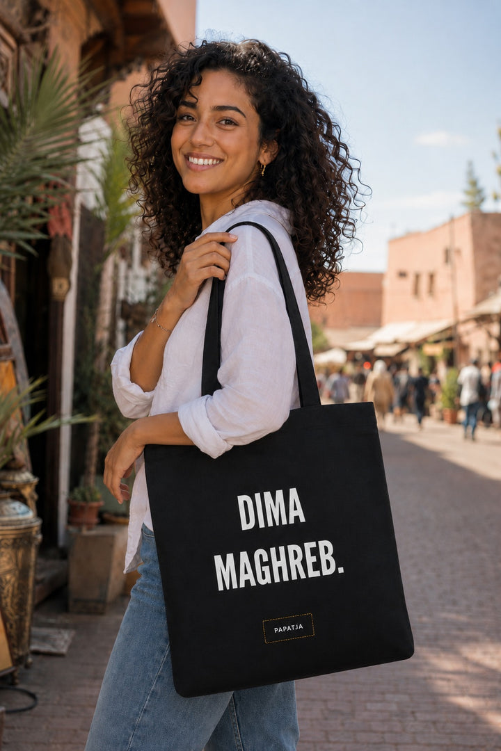 Zwarte katoenen tas met de tekst Dima Maghreb, gedragen door een Marokkaanse vrouw op een zonnige straat.
