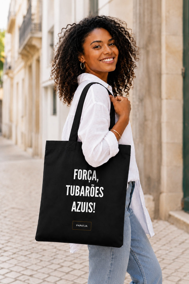 Zwarte katoenen tas met de tekst Força, Tubarões Azuis, gedragen door een Kaapverdiaanse vrouw op straat.