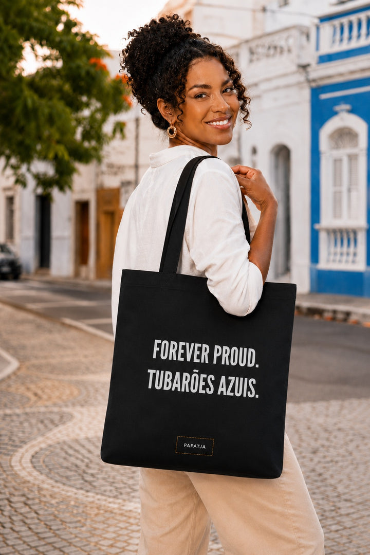 Zwarte katoenen tas met de tekst Forever Proud. Tubarões Azuis, gedragen door een Kaapverdiaanse vrouw op straat.