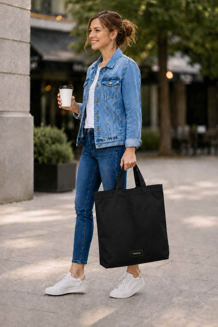 Vrouw met een zwarte PAPATJA katoenen tas met tekst, gestyled als cadeau voor dagelijks gebruik.