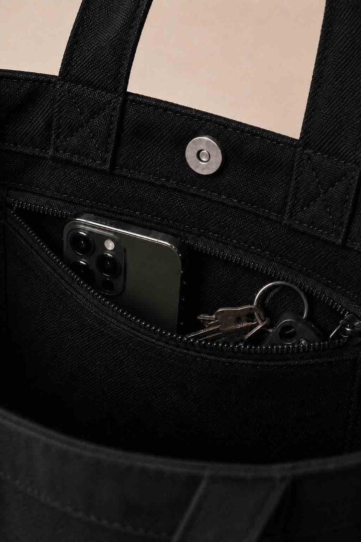 Close-up van een zwarte PAPATJA katoenen tas met binnenvak met rits, telefoon, sleutels en zilverkleurige magneetsluiting.